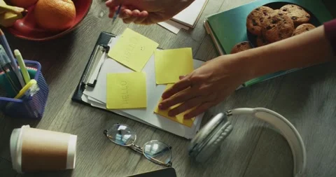 Close up a girl makes notes using a pen on yellow stickers word Hello and a 스톡 동영상 299943086