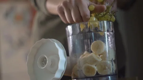 Close-up of a girl preparing a smoothie using bananas, grapes and milk.  Mixing  Stockbeeldmateriaal 120656510