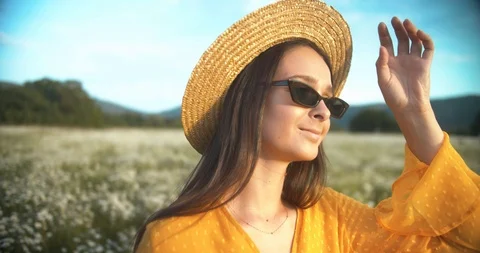 Close-up of girl in straw hat and sunglasses at sunset posing on daisy field Stock Footage 112015317