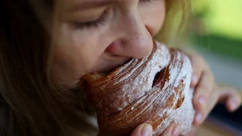 A close-up of a girl taking an appetizing bite of a croissant and chewing Stock Footage 283557254
