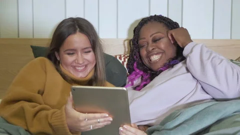 Close - Up Of Girlfriends Lying In Bed Using A Tablet Are At Home, Evening Stock Footage 139325747