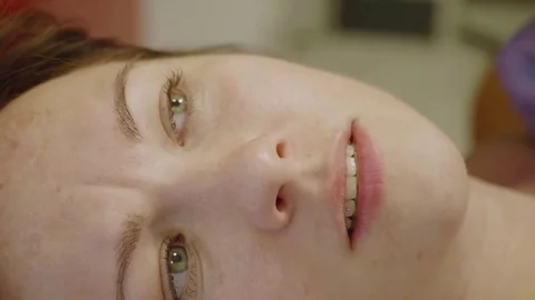 Close up of girl's face while being tattooed. Girls narrows her eyes licks her Stock Footage