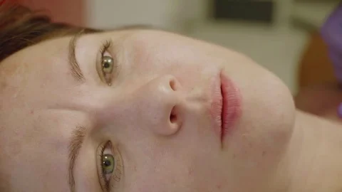 Close up of girl's face while being tattooed. Girls narrows her eyes, bites lips Video stock 77553205