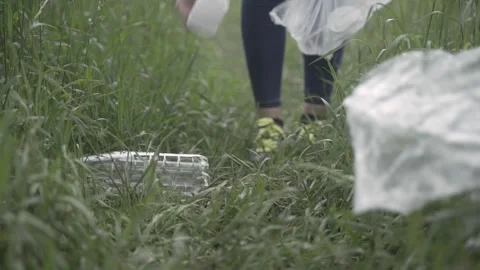 Close-up of a girl's hand picking up plastic trash from the grass. The girl  Stock Footage 242090933
