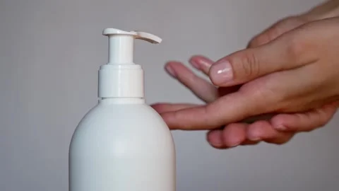 Close-up of a girl's hands applying liquid hand sanitizer in an office setting. Stock Footage 308397679
