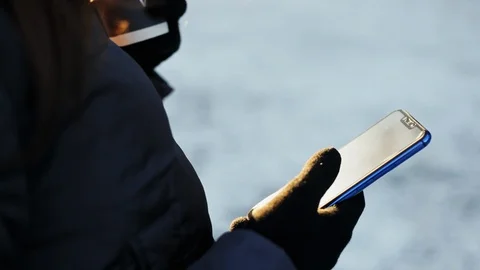 Close up of the girl's hands in gloves, using smartphone and drinking coffee Stock Footage 99102818