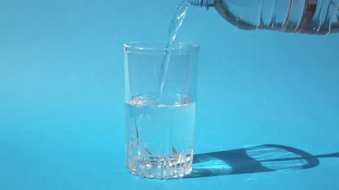 Close-up of a glass on a bright blue background, into which clean drinking water Stock Footage 165229266