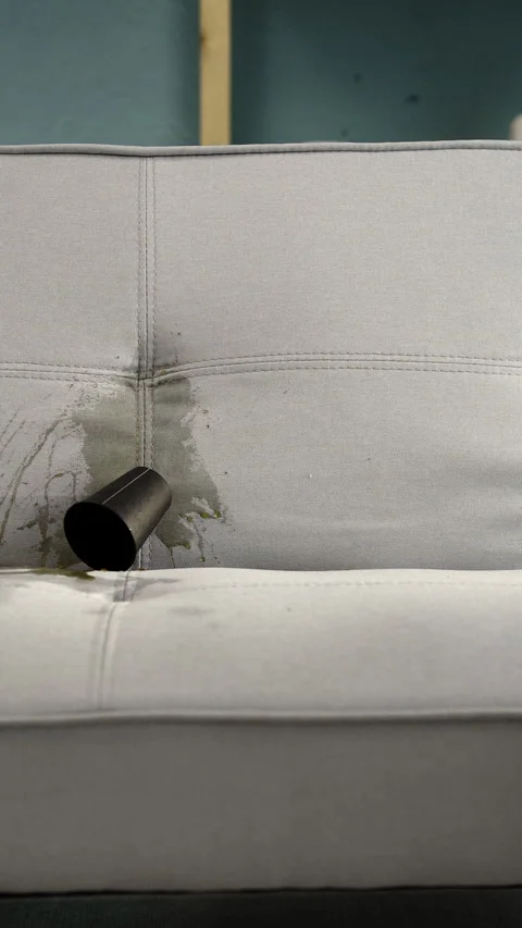 Close up of glass with coffee or tea falling on soft fabric sofa creating dirty Stock Footage 317089941