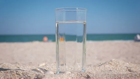 Close-up glass with drinking water standing in the sand on the beach. The girl Stock Footage 95961819