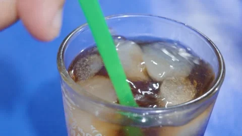 Close up of a glass of refreshing cold drink with ice cubes and green straw. Video stock 343381675