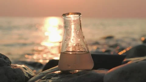 Close up of glass test sample flask of dirty water. Sunset and sea on background Stock Footage 253159927
