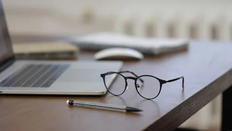 Close up glasses lie on a wooden work table with a laptop and a pen Stock Footage 146087757