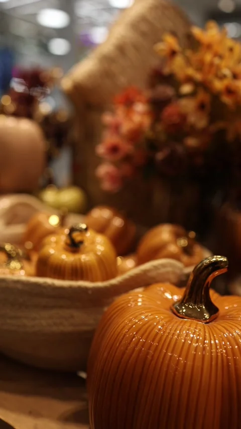 Close up of glossy ceramic pumpkin with golden stem and blurred autumn decoratio Видео 346973904