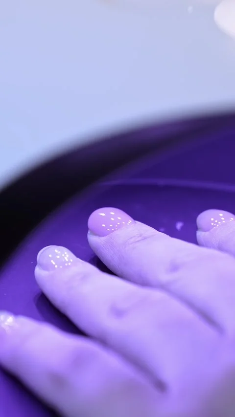 Close-up of glossy fingers curing under a UV lamp, with violet LED light Видео 333653932
