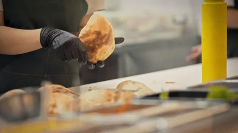 A close-up of a gloved chef using a knife to cut a bun and fill it with meat Stock Footage 340078059