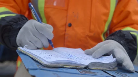 Close-up on gloved contruction worker writing in note book with pen Stock Footage 231355657