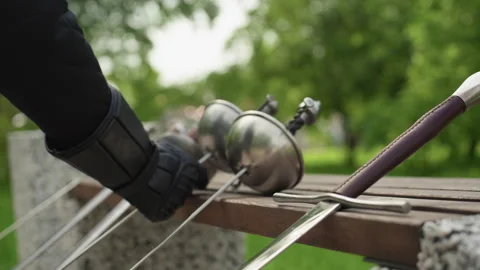 Close up of gloved hand reaching to pick fencing sword from three resting on Stock Footage 345835127