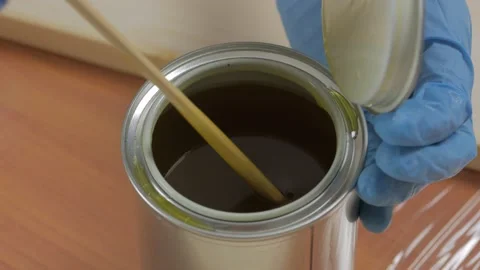 Close-up of a gloved hand using a wooden stick to mix wood processing oil Stock Footage 149405592
