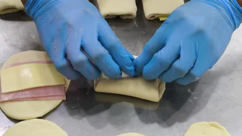 Close-up of gloved hands shaping a ham and cheese puff pastry Stock Footage 339286209