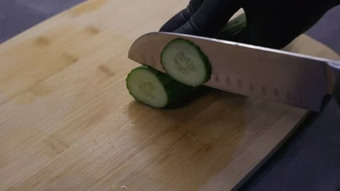 Close-up of gloved hands slicing a fresh cucumber with a kitchen knife on a Stock Footage 346858322