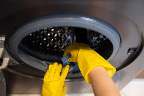 Close-up of gloved hands wiping inside washing machine drum. Stock Photos