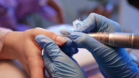 Close-up of a gloved nail technician refining a client’s fingernail with an Stockbeeldmateriaal 333650782