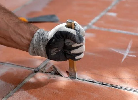 Close up of a gloved worker hand holding a chisel while removing old floor ti 写真素材