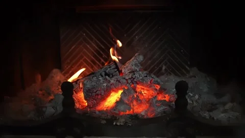 Close-up of glowing embers and small flames inside a fireplace insert, creating Stock Footage 327889648
