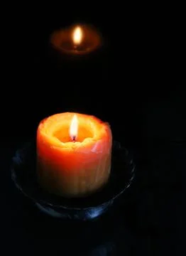 Close-up of glowing orange candle with reflection on shiny black surface Stock Photos