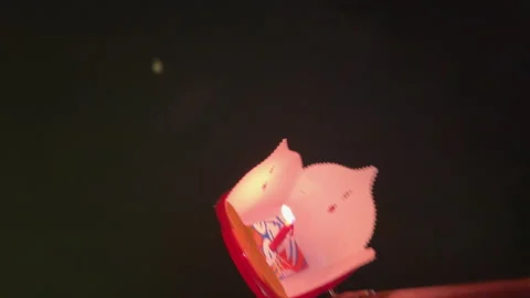 Close-up of a glowing paper lantern being lowered from a boat into Hoi An’s Stock Footage 333780447