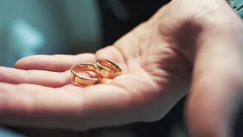 Close-up of gold wedding rings falls in hand, marriage, commitment, and eternal Stock Footage 311506247