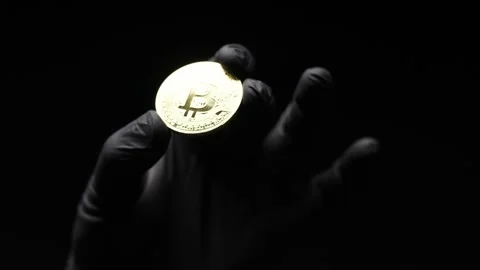 Close-up of a golden Bitcoin held in a gloved hand, symbolizing financial Stock Footage 302374603
