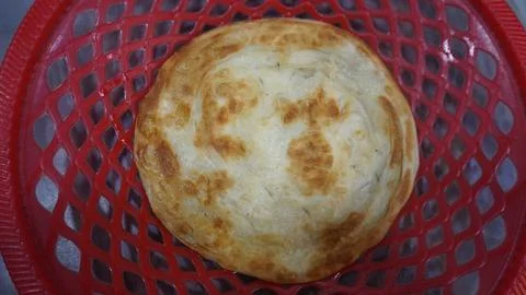 Close-up of a golden-brown circular flatbread placed on a red basket. Stock Photos