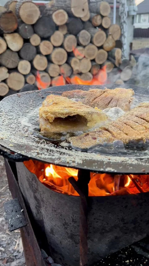 Close up of golden cornmeal fried fish pieces sizzling over an open fire griddle Stock Footage 344303046