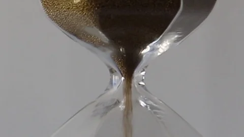 Close-up of golden sand quickly flowing through an hourglass on a white back Stock Footage 124587250