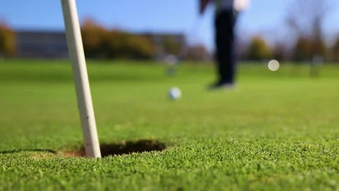 Close-up of golf ball sinking into hole with senior golfer in background Stock Footage 292017319