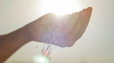 Close-up of grains falling out of a hand against the sky and sun. Stock Footage 67041544