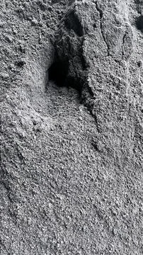 Close up of granular gray sand with a dark hollow hole and rough texture crea Stock Photos
