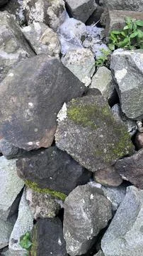 Close up of gray and dark brown rocks stacked together with patches of green Stock Photos