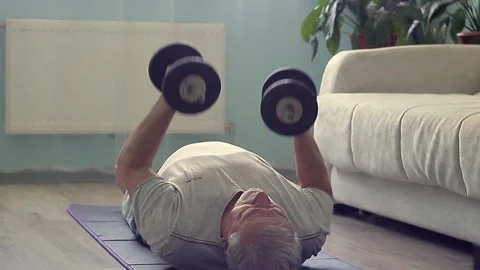 Close-up of gray-haired elderly old man doing weightlifting on yoga mat at home Stock Footage 155218833