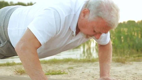 Close up of gray-haired senior old man doing push-ups on yoga mat on the beach Stock Footage 155218783