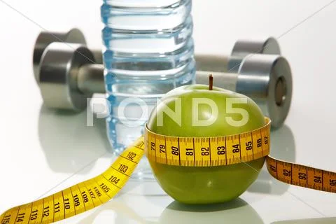 Closeup of green apple with measuring tape and two metal barbells on background Stock Photos