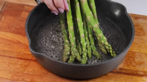 Close-up of green asparagus being placed into a pan of boiling water, hand Stock Footage 306156096
