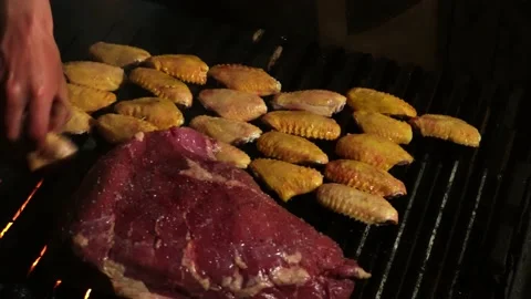 Close-up on a grill at night with a steak and chicken wings on the grill Stock Footage 164623717