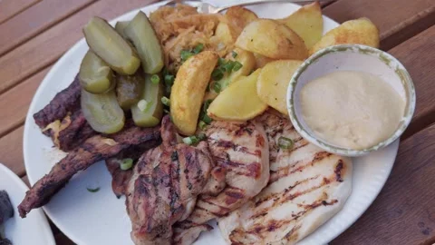 Close-Up Grilled Meat Platter with Potatoes and Pickles at Restaurant Table Stock Footage 321193197