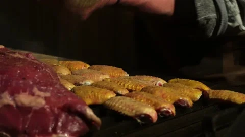 Close-up grilling chicken wings next to a meat on a grill at night in 4K Stock Footage 164623523