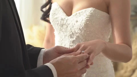 Close-up of groom placing diamond ring on bride's finger, symbolizing eternal Vidéo 261792995