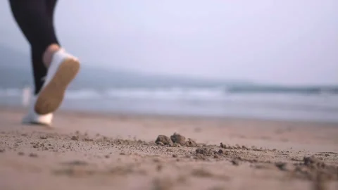 Close-up ground view of Women's legs in sneakers begins to run on the sand .. Stock Footage 286107871
