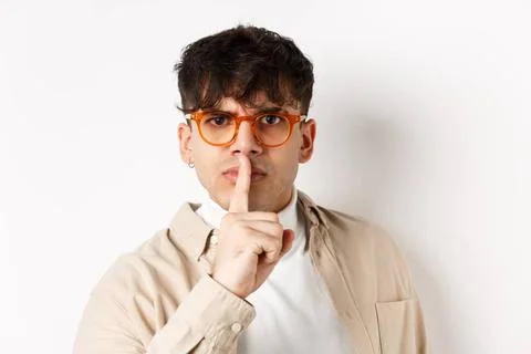 Close-up of grumpy young guy in glasses frowning and shushing, make taboo ... Stock Photos