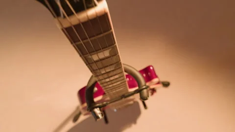 Close-up of a guitar neck and strings under warm light on a stand, viewed from Stock Footage 295112004